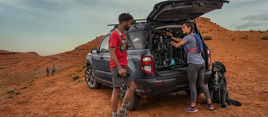 VUS Ford Bronco Sport® 2026 garé dans le désert, avec deux personnes en tenue de randonnée et leur chien à l’extérieur.