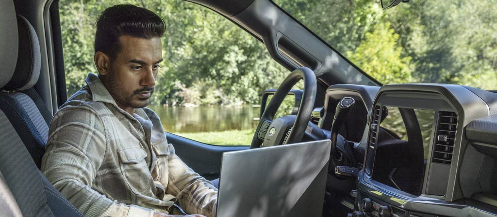 Une personne assise dans une cabine du Ford F-150® 2025 travaillant sur un ordinateur portable utilisant la surface de travail intérieure 