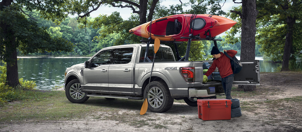 Un F-150 garé près d'un lac, avec un canoë fixé sur le toit, et une personne en train de décharger du matériel de la benne.
