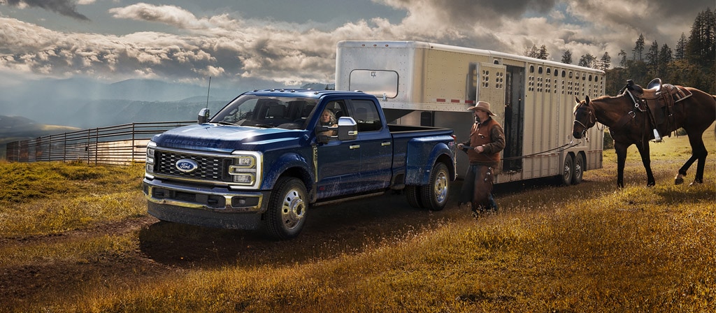 Modèle Ford Super Duty® F-450® King Ranch® 2026 en bleu argon remorquant un transporteur de chevaux sur une ferme herbeuse