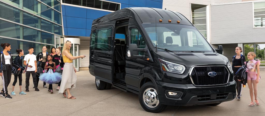 Une fourgonnette Ford Transit® 2025 stationnée avec une femme et de nombreux enfants alentour