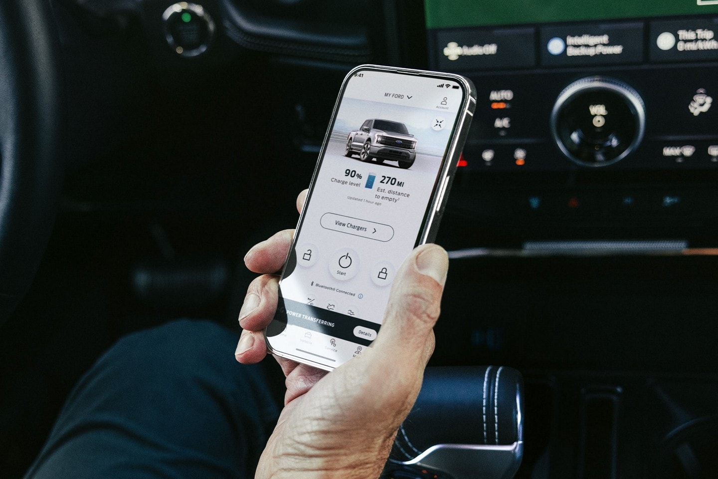 Une personne tient un téléphone intelligent affichant l’état de charge d’un véhicule.