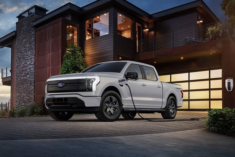 Un F-150 Lightning stationné devant une maison est branché à une borne de recharge Ford Pro