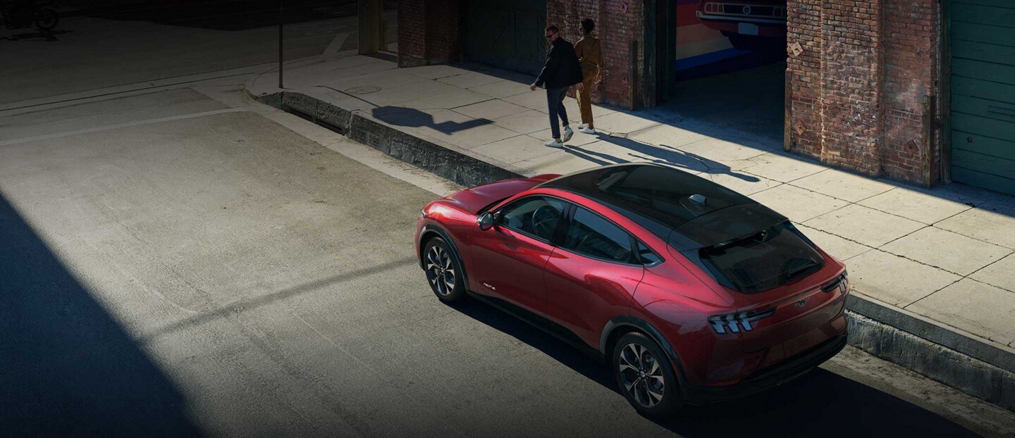 Un homme et une femme s'éloignent d'une Mustang Mach-E 2023 rouge dans un décor urbain