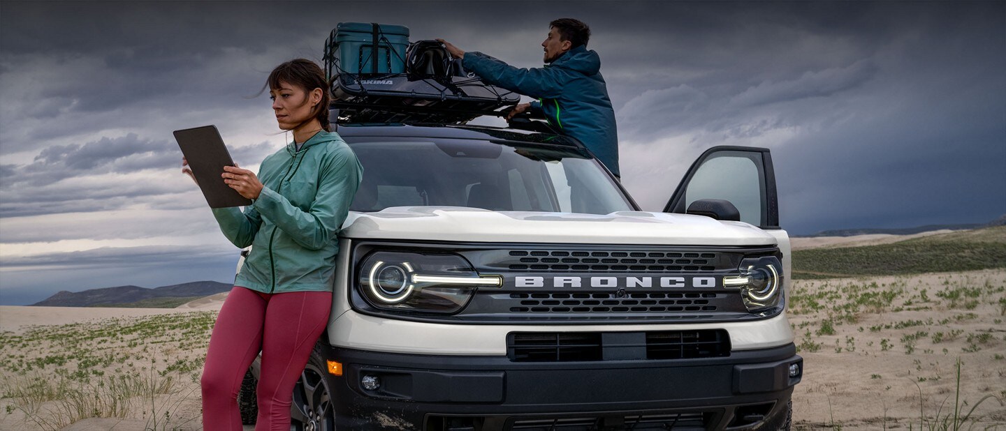 Une femme utilise une tablette lorsqu'un homme range le porte-bagages d'un Ford Bronco Sport 2023 blanc