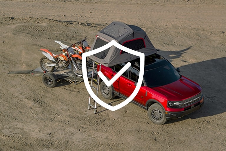 Camion Ford Ranger 2021 couleur rouge course stationné sur un sol boueux équipé d’une tente sur le toit et transportant deux motos tout-terrain