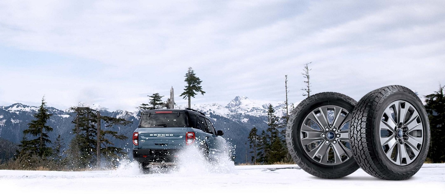 Deux pneus à côté d'un Ford Bronco Sport qui roule dans la neige