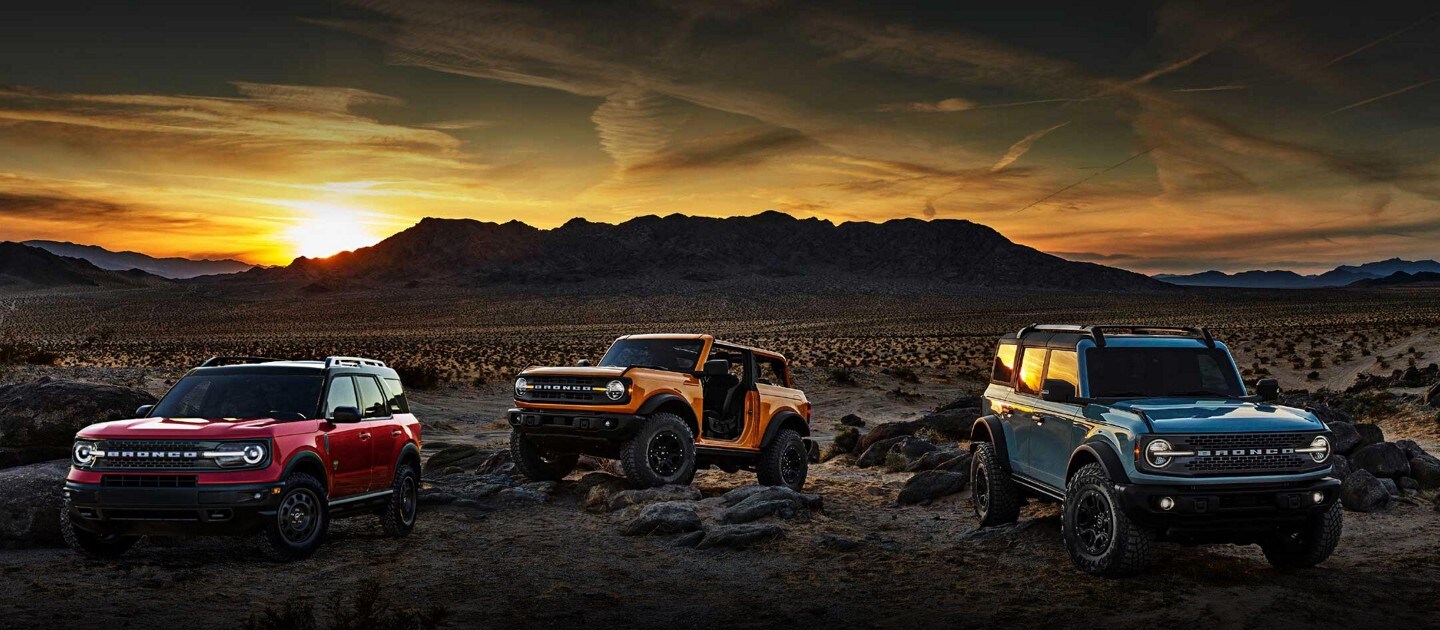 Deux VUS Ford Bronco 2022 et un VUS Bronco Sport stationné sur une colline au coucher du soleil
