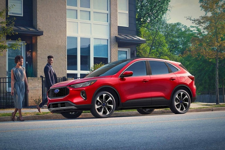 Deux personnes se tiennent près d'un Ford Escape rouge garé dans une rue de la ville