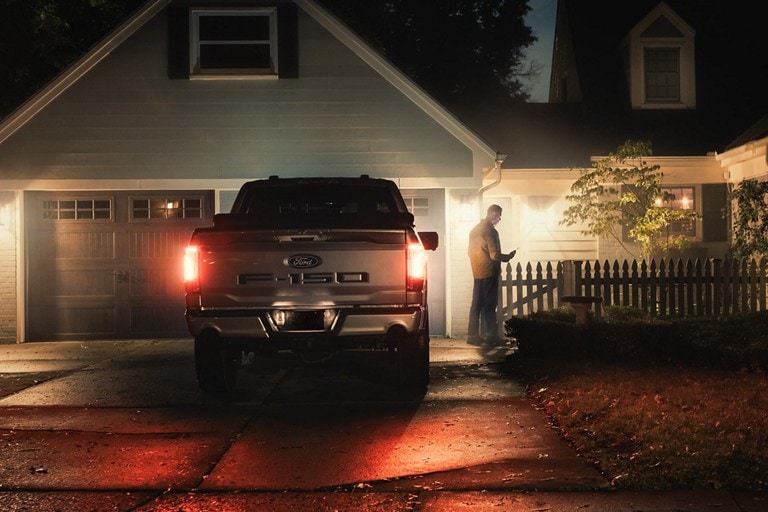 Une personne utilise un smartphone à côté d'un F 150 Lightning dans une allée résidentielle.