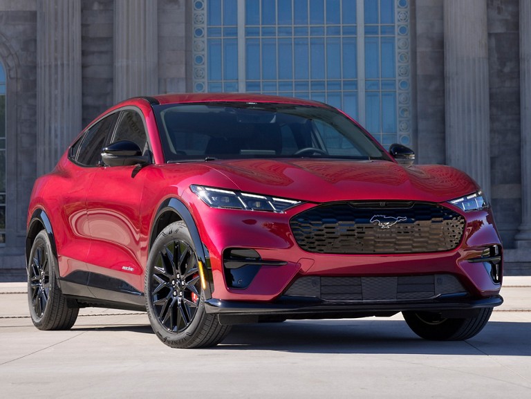 Un VUS bleu Ford Mustang Mach-E® conduit sur une route de campagne bordée d’arbres entourée de verdure.