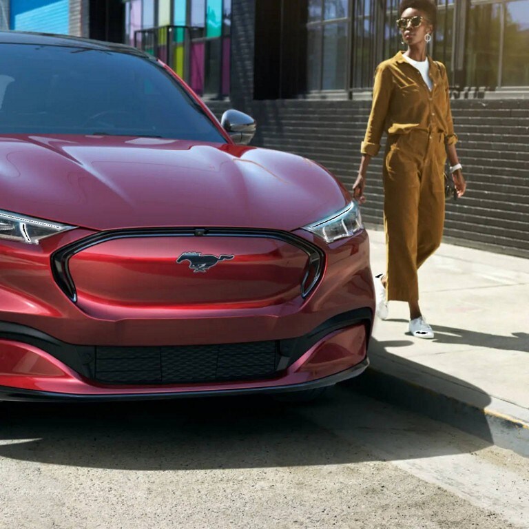 Une femme debout à côté d’une Mustang Mach E rouge