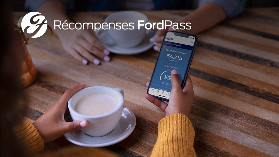 Une personne regarde l'écran d'un téléphone affichant l'application FordPass dans un café