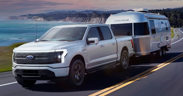 Un Ford® F-150 Lightning 2022 remorquant une caravane près d'un vaste plan d'eau