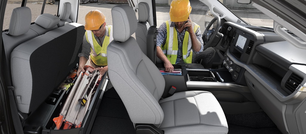 Deux travailleurs portant un casque de sécurité accèdent aux aires de rangement à l’intérieur de la cabine du Ford Super Duty® à châssis-cabine 2026