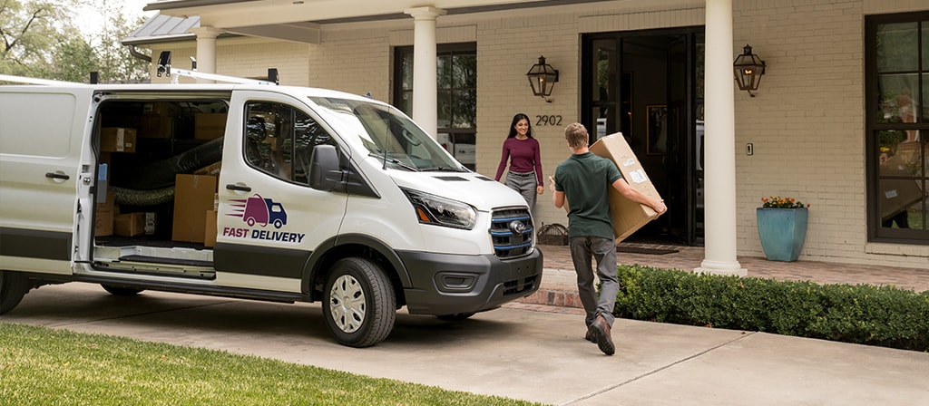 Une fourgonnette Ford E-Transit™ 2025 blanche stationnée alors que son conducteur se dirige vers une maison pour la livraison