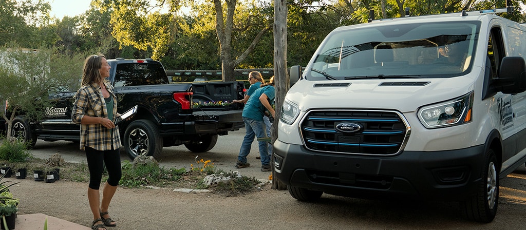 Une fourgonnette Ford E-Transit™ 2025 blanche stationnée et en train d’être chargée dans une pépinière