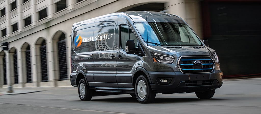 Une fourgonnette Ford E-Transit™ 2025 bleue circulant dans une rue de la ville