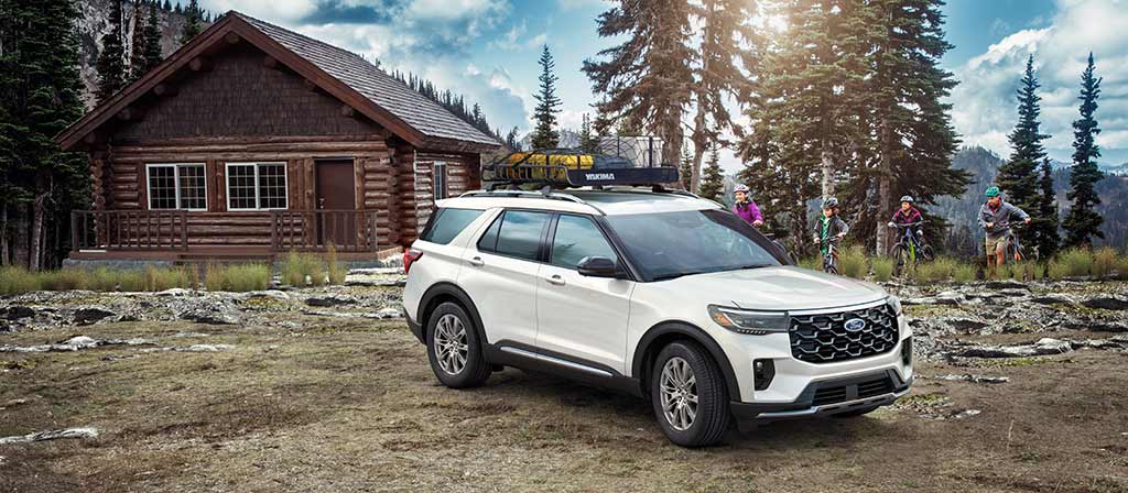 Ford Explorer® 2025 blanc stationné à l’extérieur d’une cabine rustique alors qu’une famille à vélo approche