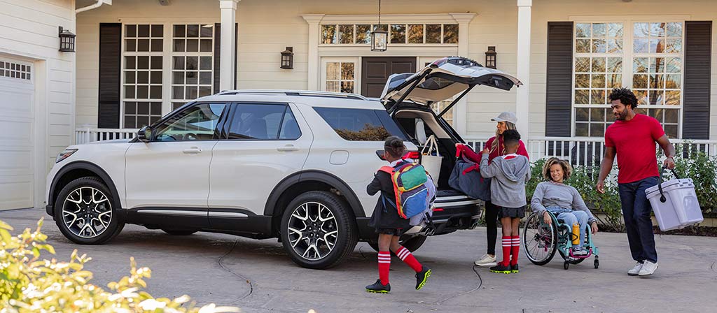 VUS Ford Explorer® 2025 stationné dans l’entrée avec une famille debout à l’extérieur du véhicule