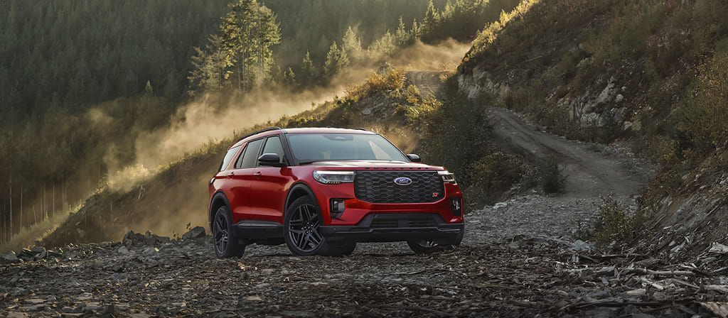 Ford Explorer® 2025 rouge stationné sur du gravier avec un paysage de forêt montagneuse en arrière-plan