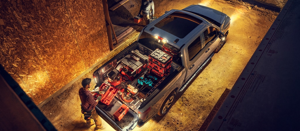 Un Ford F-150® Lightning® 2025 illuminé la nuit avec une personne sur un chantier de construction saisissant l’équipement de la caisse du camion