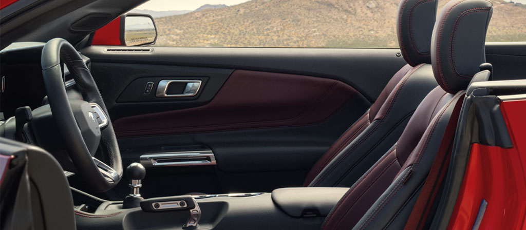 Ford Mustang® 2025 décapotable stationnée avec la portière du côté conducteur ouverte montrant l’intérieur rouge carmin en option