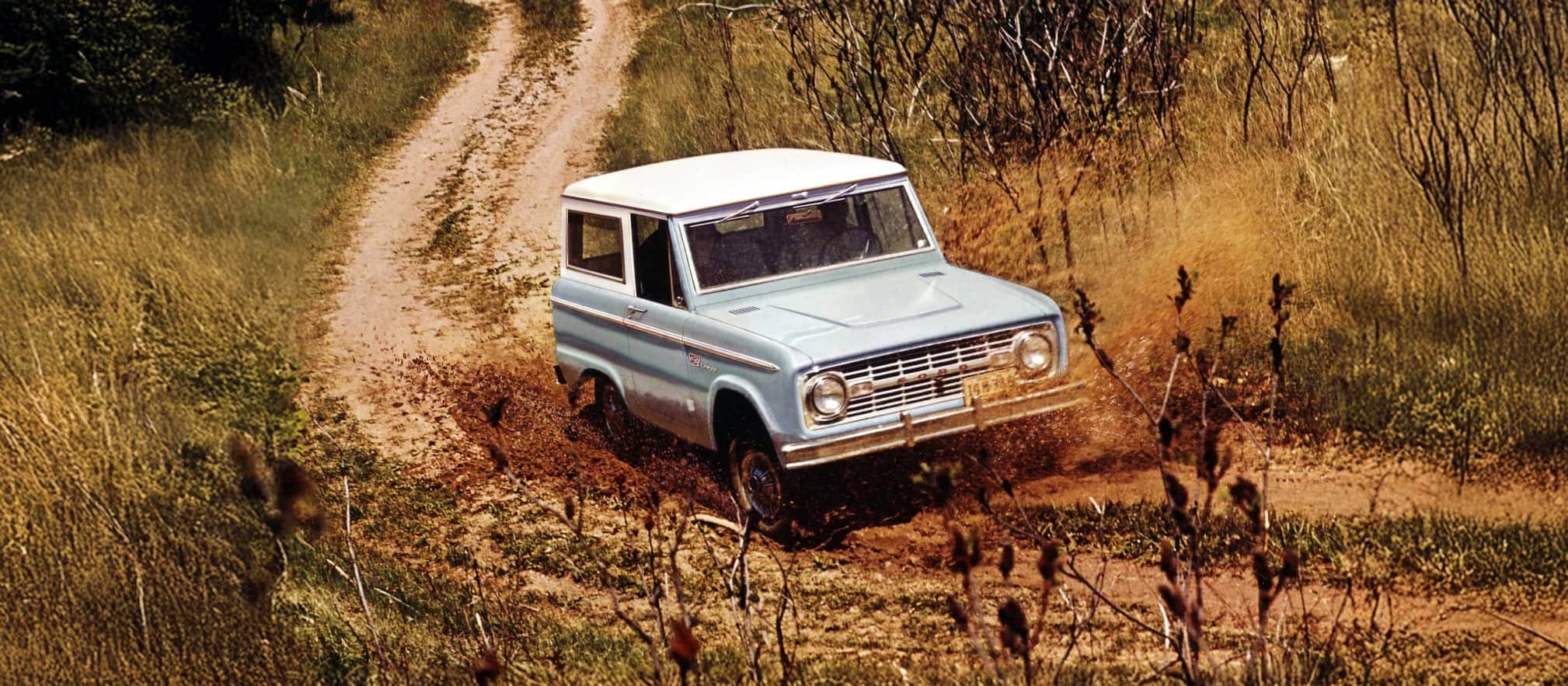 Une fourgonnette Bronco des années 1960 roulant sur un chemin de terre.