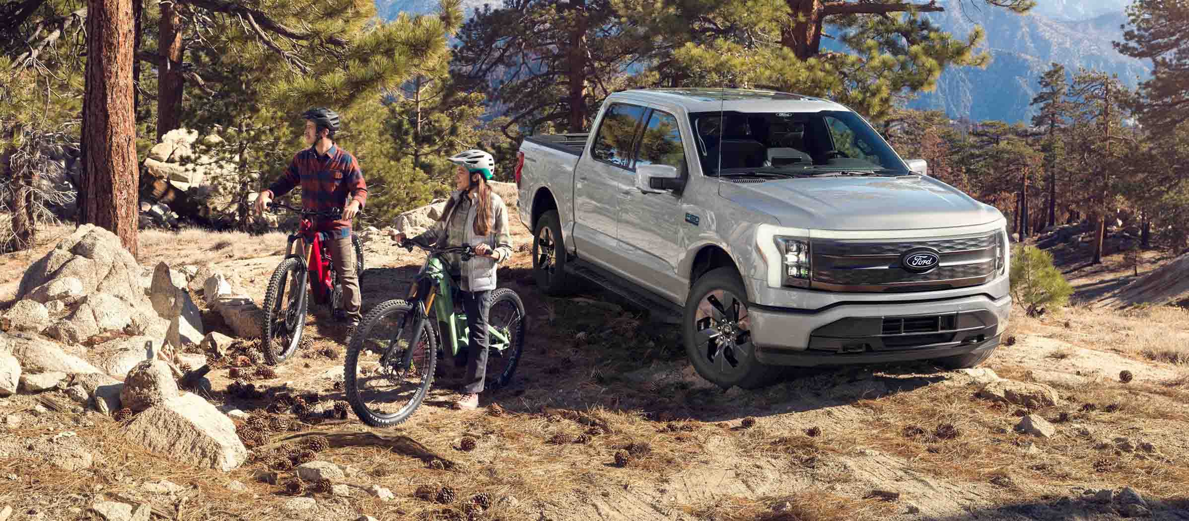 Deux personnes en VTT à côté d'un F-150 Lightning sur une colline accidentée.