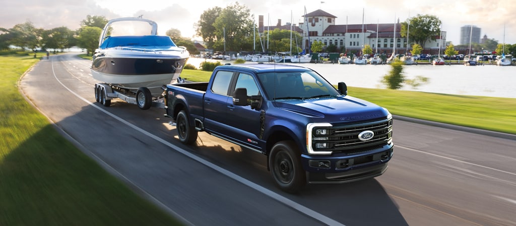 Modèle Ford Super Duty® F-350® Platinum® 2026 en bleu argon remorquant un bateau à moteur sur une route pavée