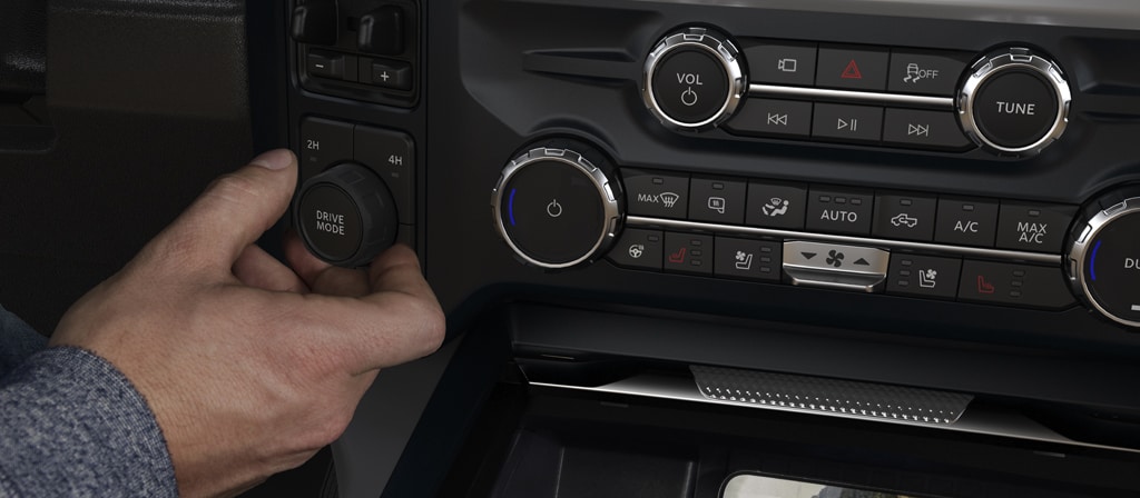 Réglage du bouton du mode de conduite à l’intérieur d’un Ford Super Duty® 2026, tandis qu’un téléphone se recharge avec le tapis de recharge sans fil