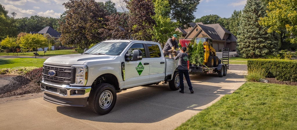 Camion Ford Super Duty® 2026 stationné dans une entrée tirant une grande remorque avec de l’équipement pour l’aménagement paysager