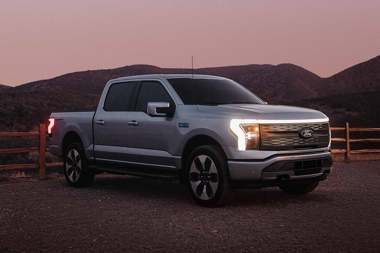 Un Ford F-150 Lightning® 2025 stationné près d’une clôture, avec les phares et la barre de lumières distinctive allumée