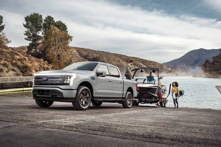 Un camion Ford F-150 Lightning® 2025 remorquant un bateau sur une remorque montant une rampe de bateau sur un lac de montagne