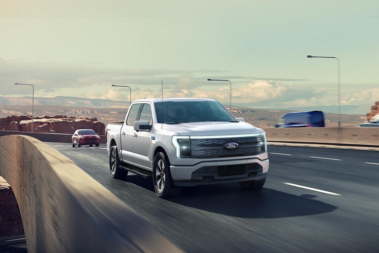 Un camion Ford F-150 Lightning® 2025 circulant sur une autoroute près d’un paysage montagneux spectaculaire
