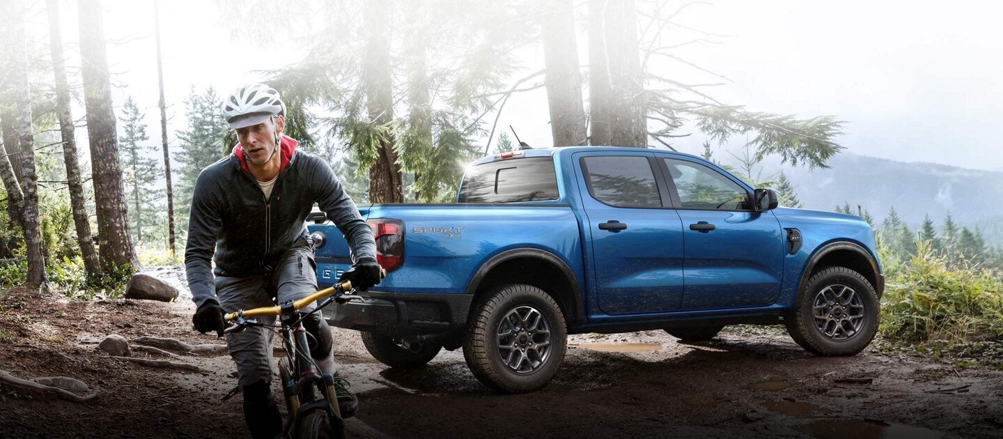 Un Ford Ranger® XLT 2024 doté d’un ensemble d’allure sportive stationné sur une colline boueuse près d’une personne sur un vélo de montagne