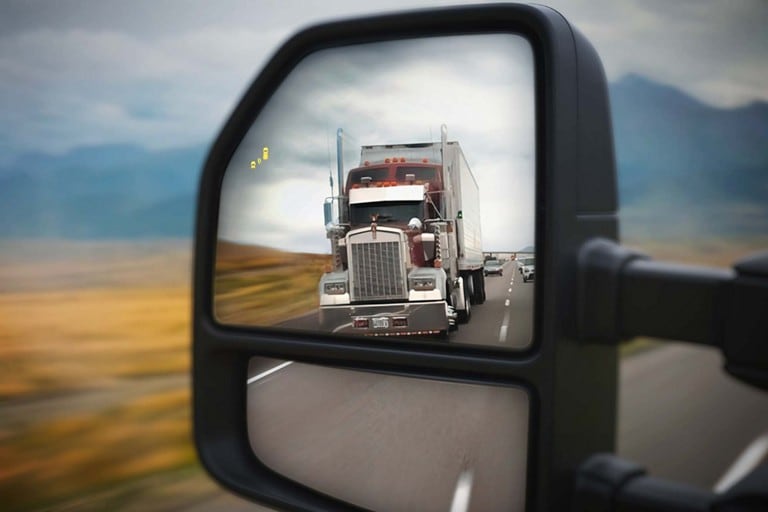 Gros plan des rétroviseurs de remorquage mettant en évidence l’icône du système d’alerte pour angle mort avec une semi-remorque dans le reflet