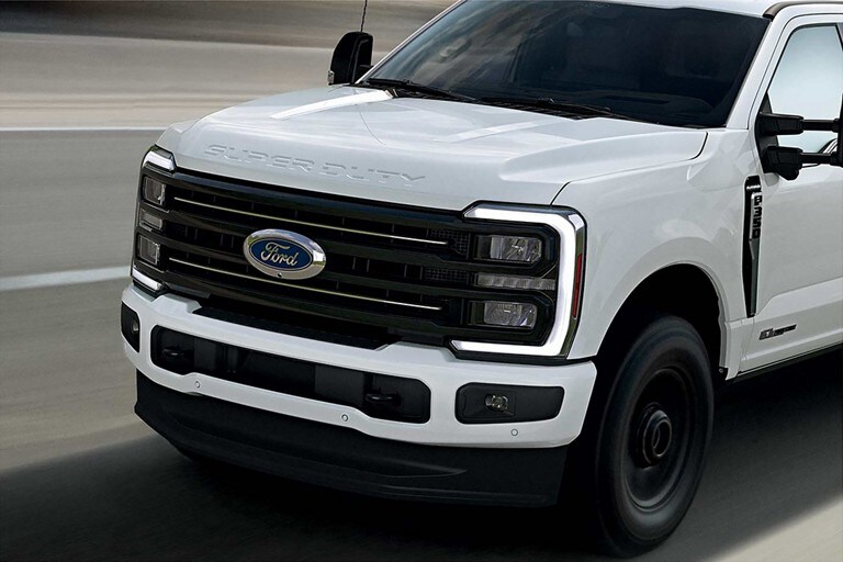 L’avant d’un modèle Ford Super Duty® Platinum® TREMOR™ 2025 en blanc Oxford circulant sur une route pavée