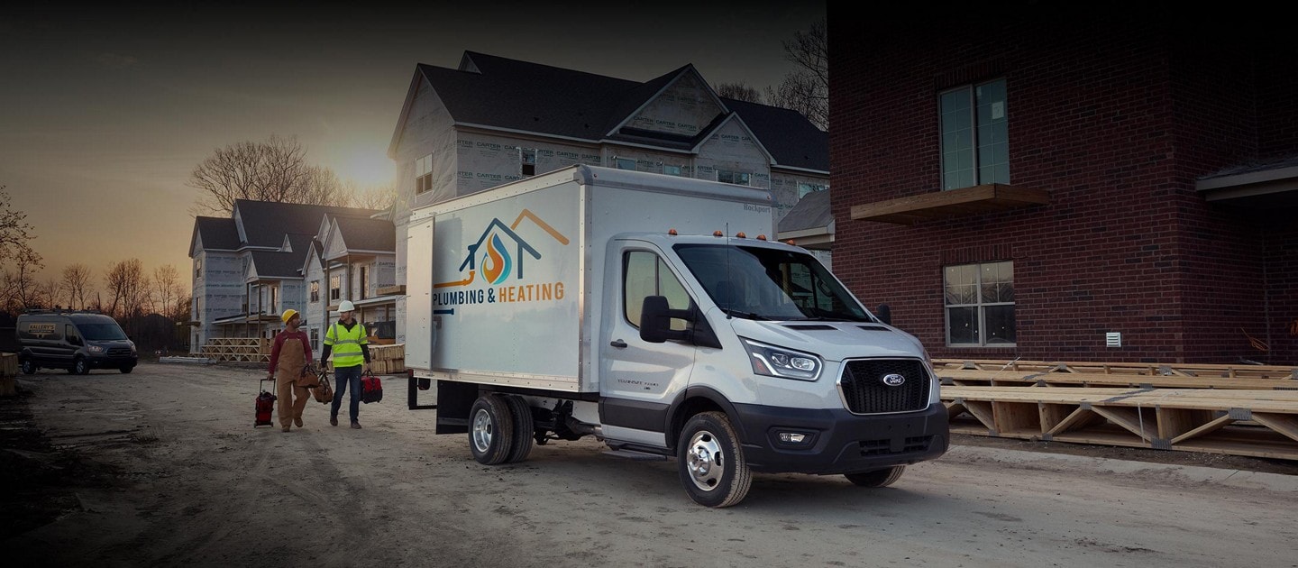 Deux travailleurs de la construction marchant près d’un modèle Ford Transit® châssis-cabine 2025 avec aménagement de camion fourgon sur un chantier