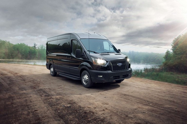 Une fourgonnette Ford Transit® 2024 en noir agate avec traction intégrale emprunte une route de terre
