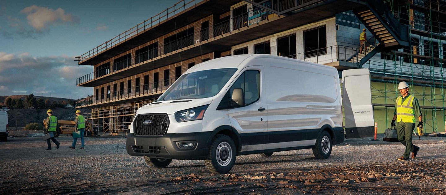 Fourgonnette Ford Transit® 2025 stationnée devant un chantier de construction avec des travailleurs à proximité