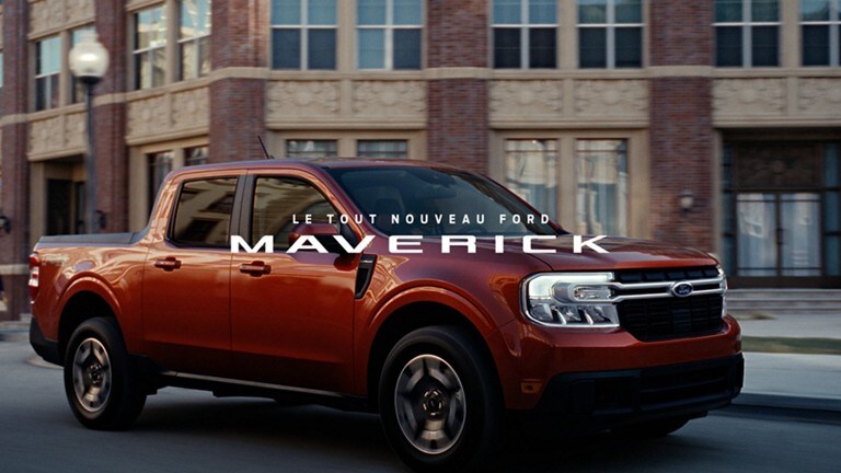 Ford® Maverick LARIAT 2022 passant devant un bâtiment en briques et les mots " Le tout nouveau Ford Maverick " superposés à l'image.