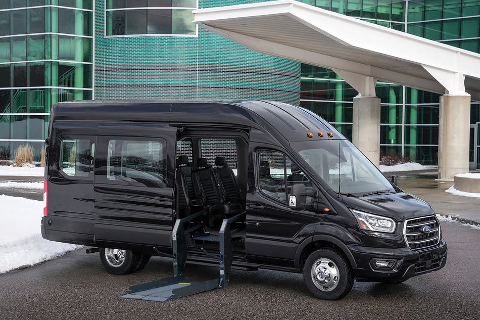 Un Ford Transit noir avec sa porte latérale ouverte montrant une plate-forme élévatrice pour fauteuil roulant.