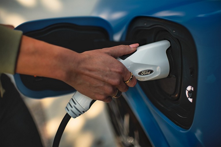 Une personne branche un chargeur à un VÉ Ford. 