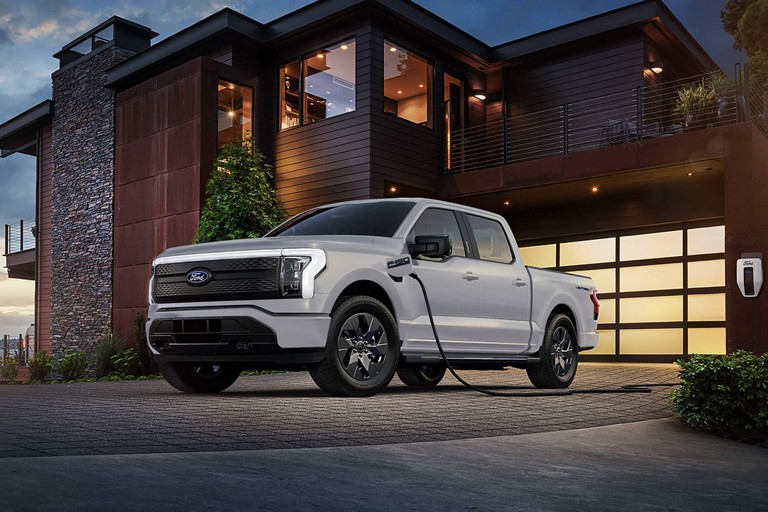 Un F-150 Lightning stationné devant une maison est branché à une borne de recharge Ford Pro