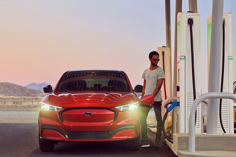 Une personne se tient à côté d'une Ford Mustang Mach E rouge pendant qu'elle se recharge