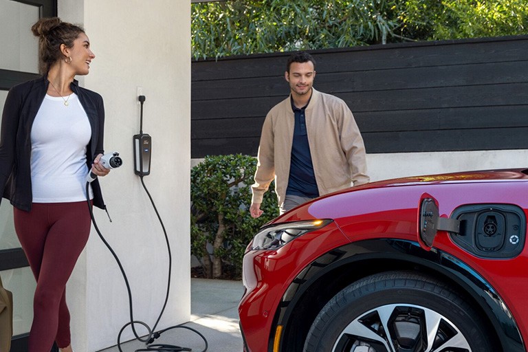 Une personne tient un câble de charge près d'une Ford Mustang Mach E dont le port de charge est ouvert