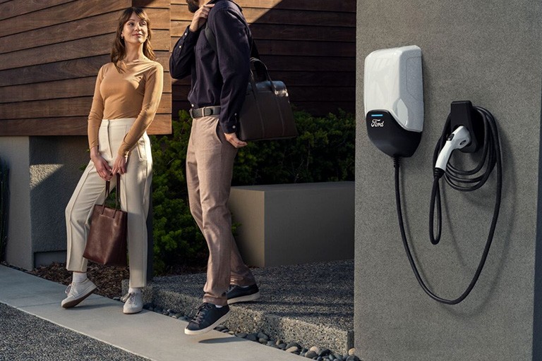 Un couple se tient près de l'entrée d'une maison à côté d'un chargeur Ford installé sur le mur