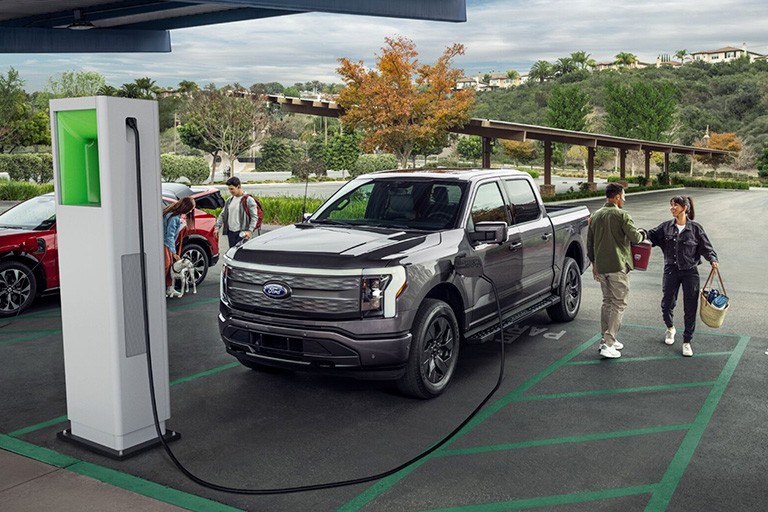 Un couple se tient à côté d'un Ford F 150 Lightning stationné dans une station de recharge rapide