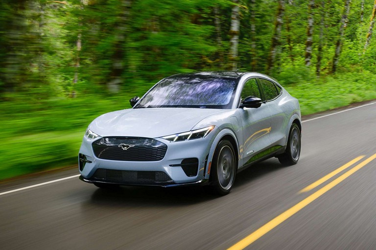 Une Mustang Mach-E sur une route bordée d’arbres.